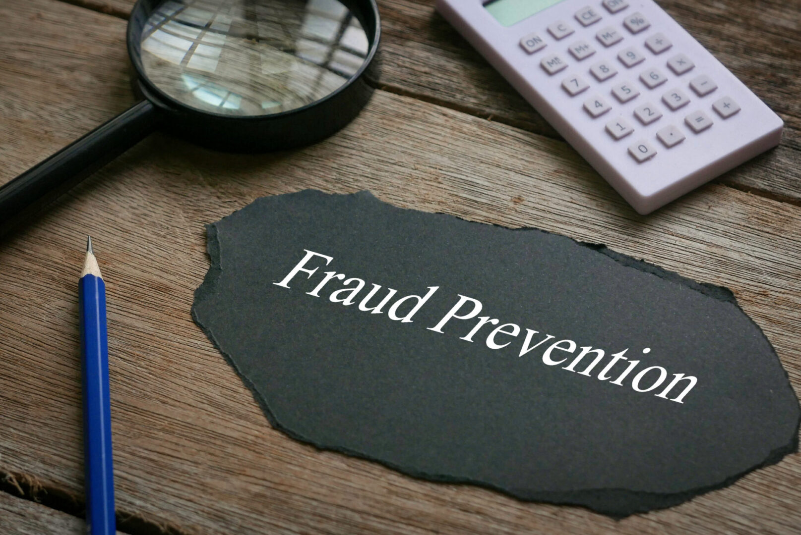 Calculator,magnifying glass,pencil and piece of black paper written with Fraud Prevention on wooden background.