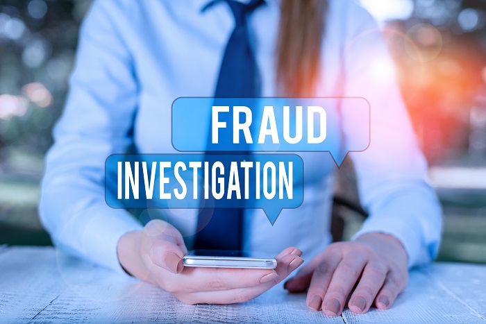 Word writing text Fraud Investigation. Business concept for process of determining whether a scam has taken place Female business person sitting by table and holding mobile phone.